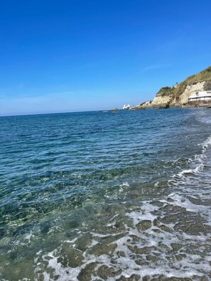 Ein Küstenstrand mit klarem Wasser, felsigem Ufer und Gebäuden auf der Klippe.
