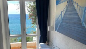 A hotel room with a bed, a painting of a pier, a view of the sea, and a balcony with a view of the sea.