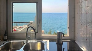 A kitchen with a large window offering a view of the sea.