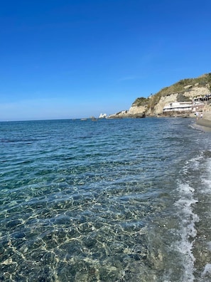 A beach with clear water, a rocky shoreline, and buildings on the cliff. - SEA VIEW apartment CAVA dell’ISOLA (Forio)• Elowen (Forio)