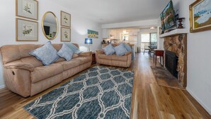 Un salon avec un canapé beige, un tapis à motifs, une cheminée et des œuvres d’art encadrées accrochées aux murs.
