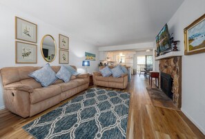 Ein Wohnzimmer mit beiger Couch, einem gemusterten Teppich, einem Kamin und gerahmten Kunstwerken an den Wänden.