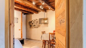 A dining area with a stone wall, wooden ceiling beams, and a table with chairs. - Casa Daisy with direct beach access, AC and Wifi (Dervio)