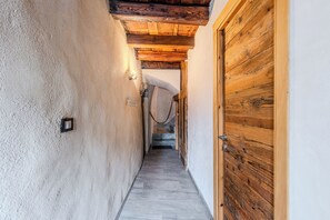 Ein schmaler Gang mit einer Holztür auf der rechten Seite, einer strukturierten Wand links und einer Decke mit freiliegenden Balken.