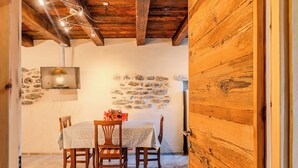A dining area with a stone wall, wooden ceiling beams, a table with chairs, and a hanging light fixture. - Casa Daisy with direct beach access, AC and Wifi (Dervio)