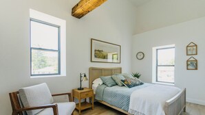 Une chambre à coucher avec un lit, une chaise, une table de chevet, une fenêtre et une horloge murale.