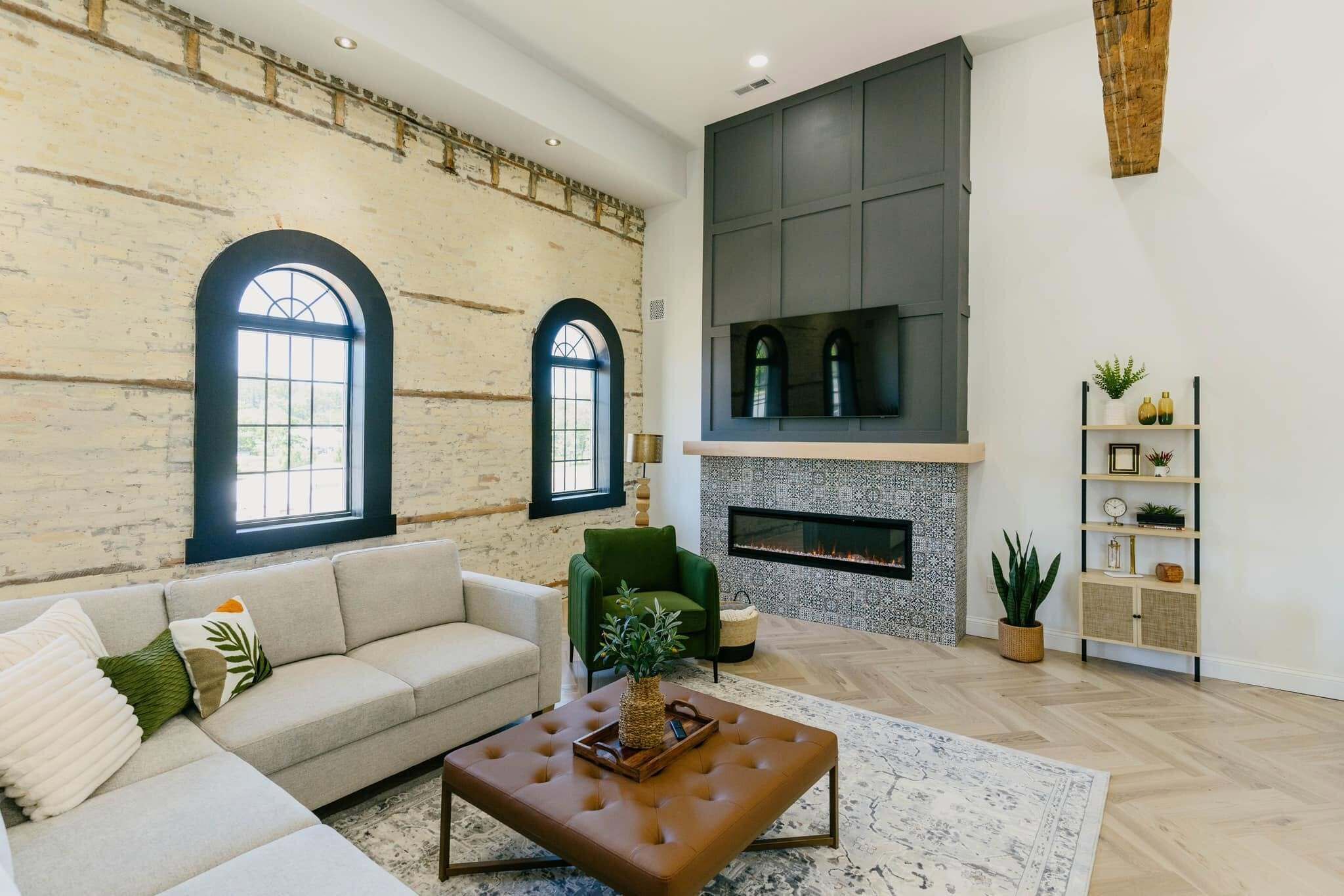 A living room with a sofa, armchair, fireplace, and a TV mounted on the wall.