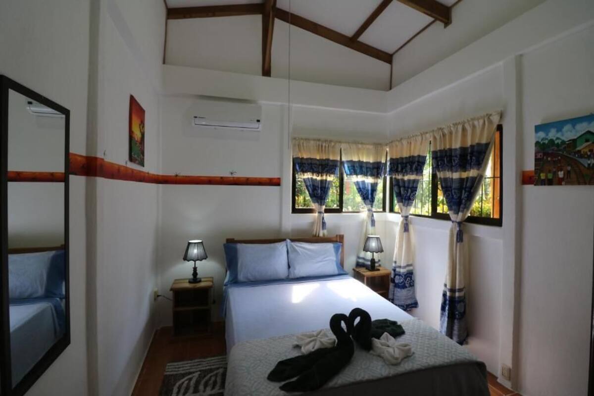 Ein Schlafzimmer mit einem Bett, zwei Nachttischen inklusive Lampen, einem Fenster mit Vorhängen und einem Spiegel an der Wand.