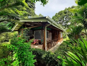 Eine Holzhütte mit überdachter Veranda, umgeben von üppiger Vegetation.