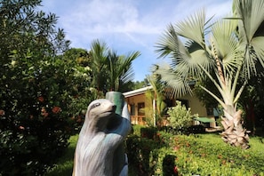 A garden with a sculpture, palm trees, and a building with a balcony. - Casas New Caribe Point (Cahuita)