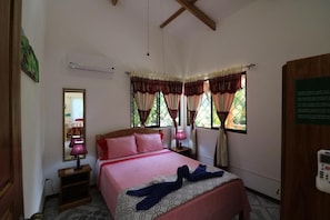 Un dormitorio con cama, mesitas de noche, espejo, cortinas y un equipo de aire acondicionado.