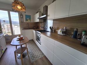 A modern kitchen with a stove, oven, and a dining area with a table and chairs. - Bright apartment with balcony in Ajaccio (Ajaccio)