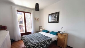A bedroom with a bed, a wooden cabinet, a nightstand, a hanging lamp, a framed picture, and a window with curtains. - Bright apartment with balcony in Ajaccio (Ajaccio)
