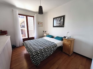 A bedroom with a bed, a wooden cabinet, a nightstand, a hanging lamp, a framed picture, and a window with curtains. - Bright apartment with balcony in Ajaccio (Ajaccio)
