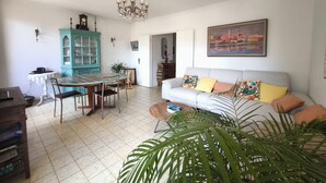 A dining area with a table and chairs, a teal cabinet, a chandelier, a sofa with colorful cushions, and a large plant. - Bright apartment with balcony in Ajaccio (Ajaccio)
