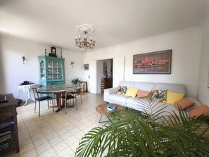 A dining area with a table and chairs, a teal cabinet, a chandelier, a sofa with colorful cushions, and a large plant. - Bright apartment with balcony in Ajaccio (Ajaccio)