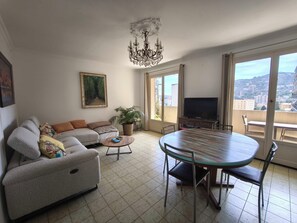 A living room with a sofa, a coffee table, a TV, and a balcony with a view. - Bright apartment with balcony in Ajaccio (Ajaccio)
