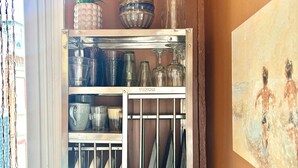 Um armário de cozinha com copos, uma abacaxi e um quadro na parede.