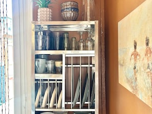 Ein Küchenschrank mit Gläsern, einer Ananas und einem Bild an der Wand.
