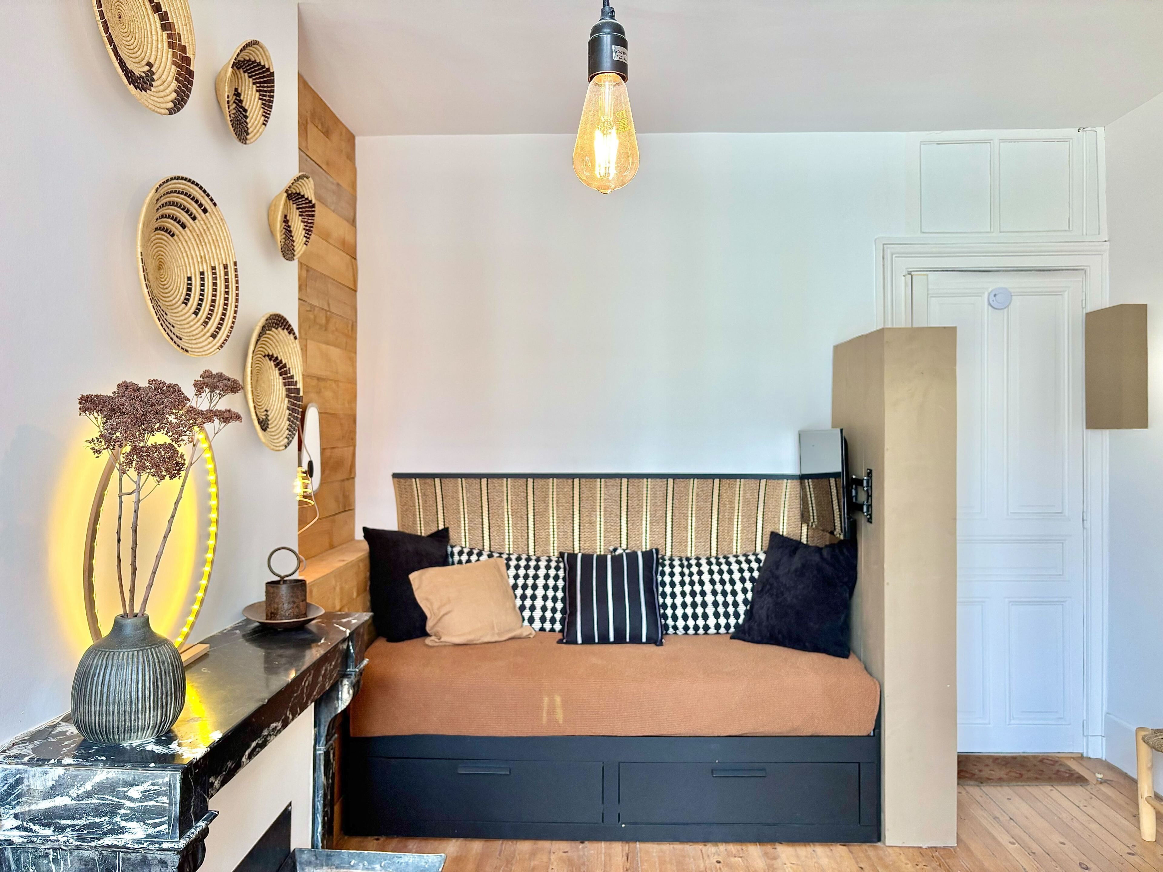 A bedroom with a bed, a bedside table, a lamp, a wall-mounted light fixture, and a door.