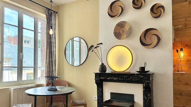 Quarto com lareira, espelho redondo e mesa com cadeiras.