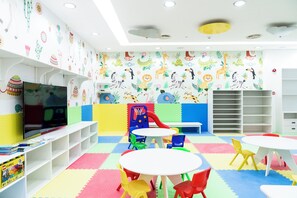 Sala de juegos infantil con paredes coloridas, televisor, espacio para jugar y asientos.