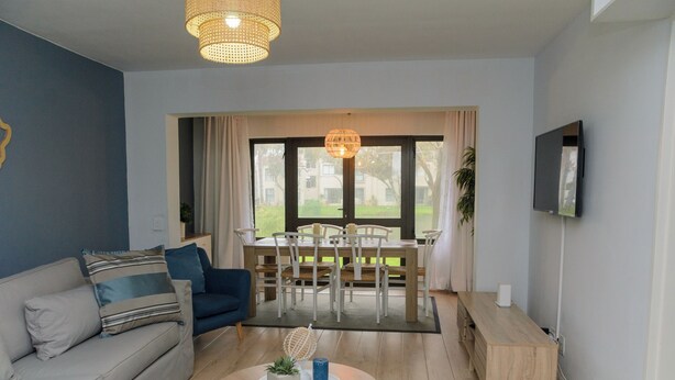 Una sala de estar moderna con un sofá, una mesa de centro, una mesa de comedor con sillas y un televisor montado en la pared.