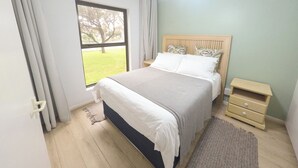 Un dormitorio con cama, mesita de noche, ventana con cortinas y ventilador de techo.