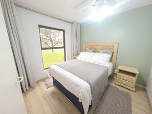 Ein Schlafzimmer mit einem Bett, einem Nachttisch, einem Fenster mit Vorhängen und einem Deckenventilator.