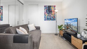 Ett modernt vardagsrum med en grå soffa, en platt-TV, en golvlampa och abstrakt konst på väggen.