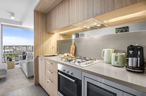 A modern kitchen with a gas stove, oven, and coffee maker. - Poolside 2-bed Apartment in South Yarra (Melbourne)