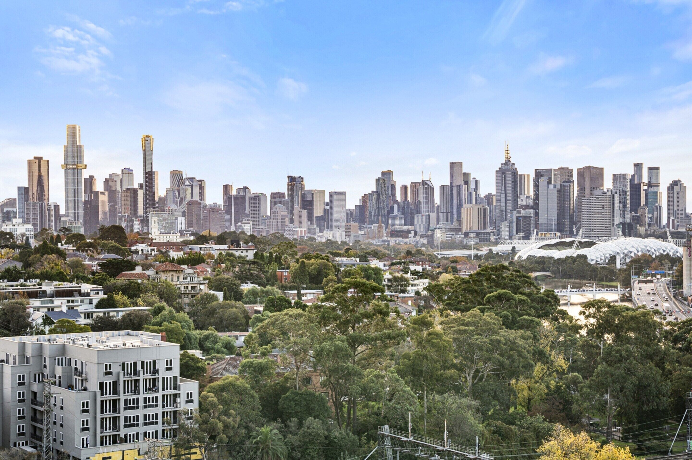 Une vue sur les toits d’une ville, avec des bâtiments modernes, un stade et des espaces verts environnants.