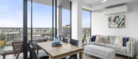 Una sala de estar moderna con comedor, ventanas amplias y vista a la ciudad.