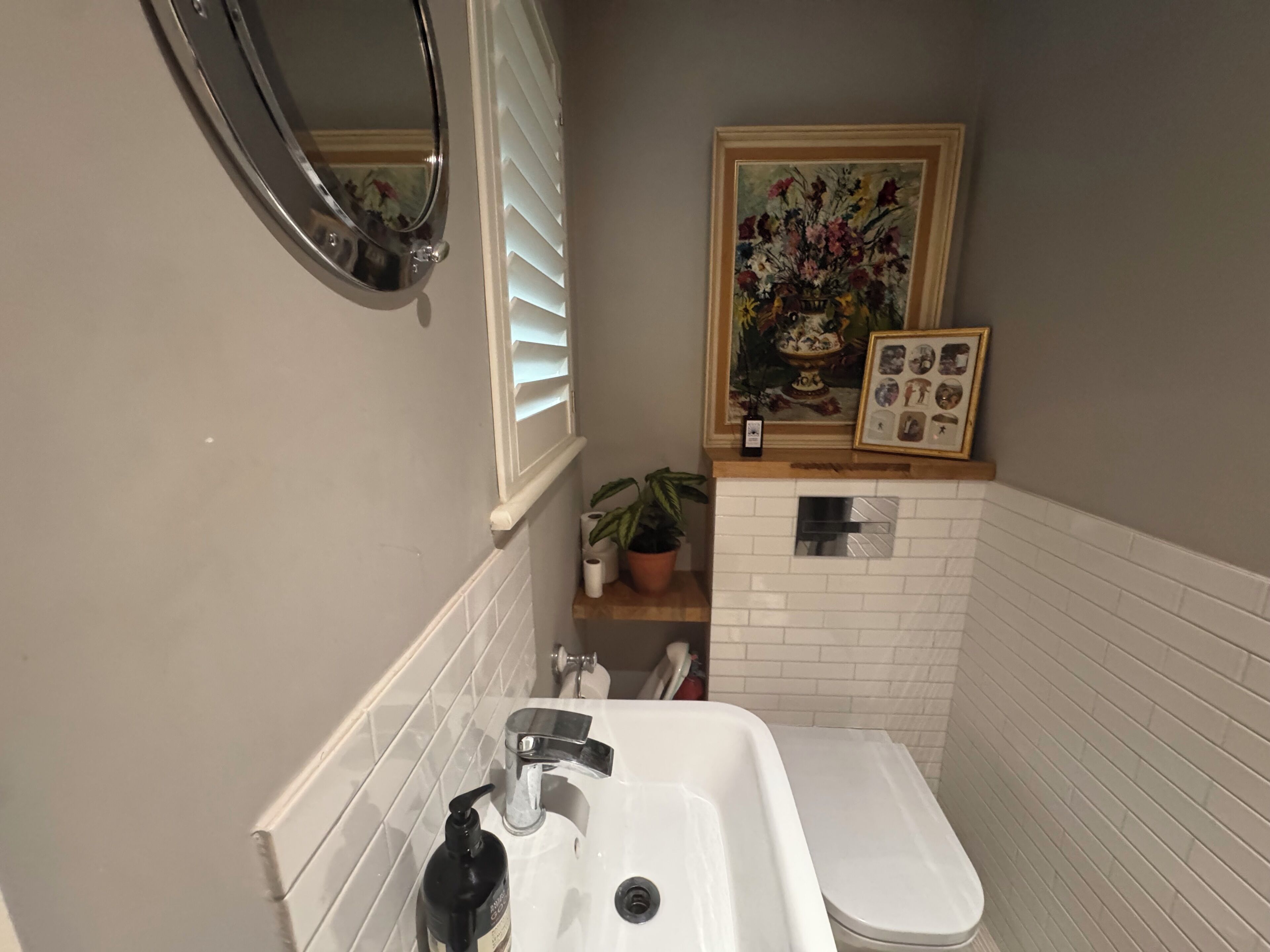 Et badeværelse med en hvid vask, et spejl, et toilet og et indrammet blomsterbillede på væggen.