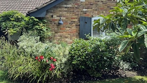 A brick house with a tiled roof, a small garden with red flowers, and a sign on the roof. - A charming English country home set in a beautiful village 28 miles from London! (Penn)