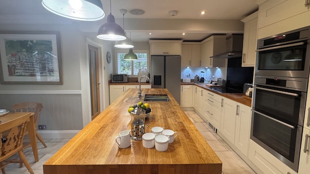 A modern kitchen with a wooden island, stainless steel appliances, pendant lighting, and a dining area with a wooden table and chairs. - A charming English country home set in a beautiful village 28 miles from London! (Penn)