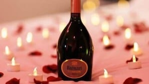 A bottle of Ruinart champagne on a bed with candles and rose petals.