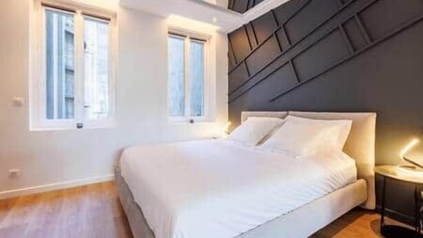 A bedroom with a bed, two windows, a nightstand, and a modern headboard.