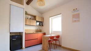 Eine kompakte Küche mit Kühlschrank, Spüle und Mikrowelle. Ein Essbereich mit Tisch und Stühlen ist ebenfalls vorhanden.