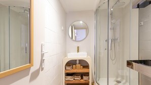 Ein modernes Badezimmer mit einer gläsernen Duschkabine, einem runden Spiegel und einer beige gefärbten Waschtischkommode mit Stauraum.
