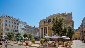 Ein Platz mit Außenbestuhlung, ein markantes Gebäude mit Säulen und ein strahlend blauer Himmel.