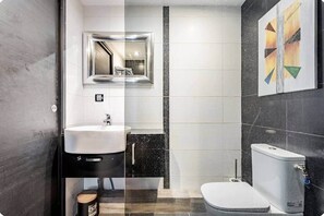 A modern bathroom with a sink, mirror, toilet, and a wall-mounted artwork. - 1-bedroom apartment on the Corniche (Marseille)