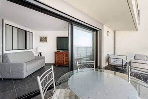 A modern living room with a sofa, a TV, a wooden cabinet, and a balcony with a glass table and chairs. - 1-bedroom apartment on the Corniche (Marseille)