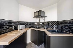 A modern kitchen with black tiled backsplash, stainless steel appliances, and a wooden countertop. - 1-bedroom apartment on the Corniche (Marseille)