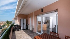 Ein Balkon mit Holztisch und -stühlen, einem Grill und einer Glasschiebetür, die zu einer Küche führt.