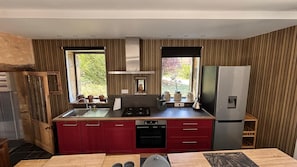 A compact kitchen with a stove, sink, and refrigerator, wooden paneling, and a window with a view of greenery. - Charming gite with spa in the heart of the Périgord Noir. Ideal for families. (Campagne)