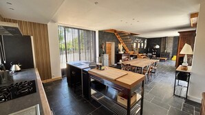 A modern kitchen with a central island, a dining area with a wooden table, and a staircase leading to an upper level. - Charming gite with spa in the heart of the Périgord Noir. Ideal for families. (Campagne)
