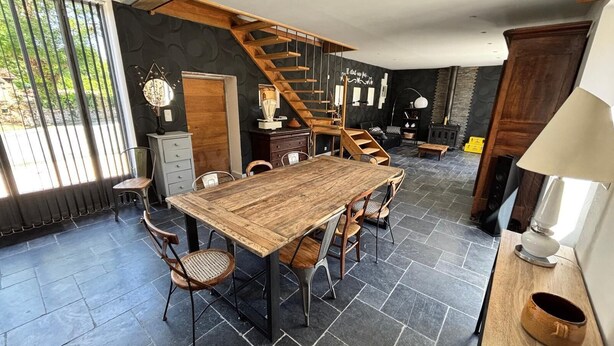 A spacious dining area with a large wooden table and chairs, a staircase, and a stone-tiled floor. - Charming gite with spa in the heart of the Périgord Noir. Ideal for families. (Campagne)