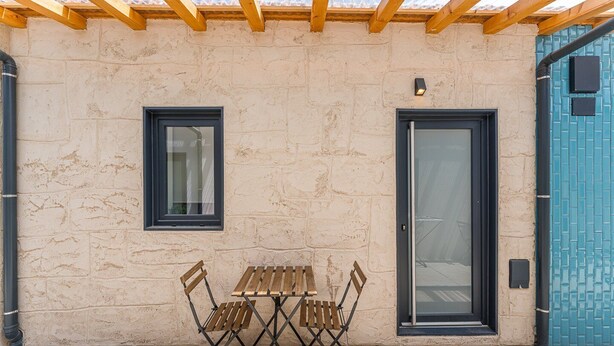 En bygning med udvendig træpergola, et bord med stole, en dør og et vindue.
