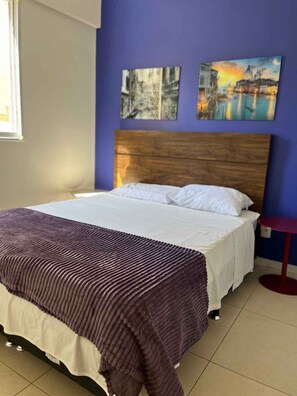 A bedroom with a bed, a wooden headboard, a purple wall, and two paintings. - LK Santo Antônio 1 (Belo Horizonte)